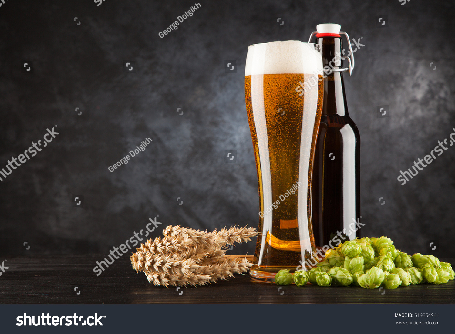 Pint glass of lager next to a swing-top brown beer bottle with wheat and hops on a dark moody background