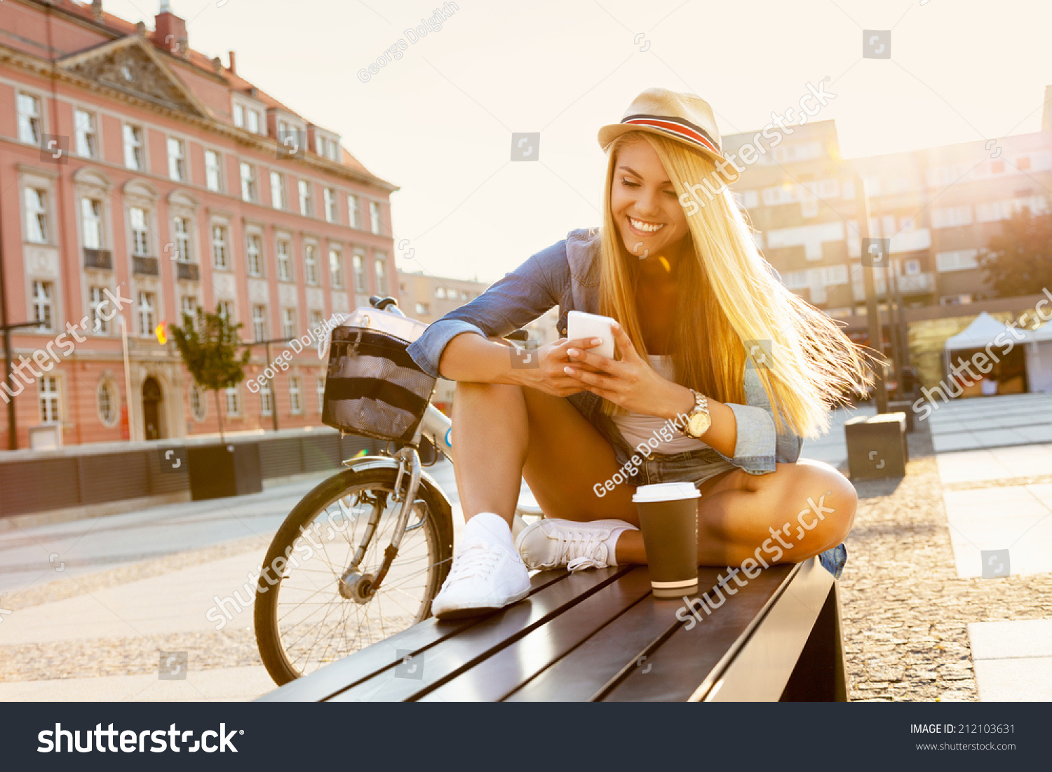 Stylish young woman with a bicycle, sitting on a bench in a sunlit city street