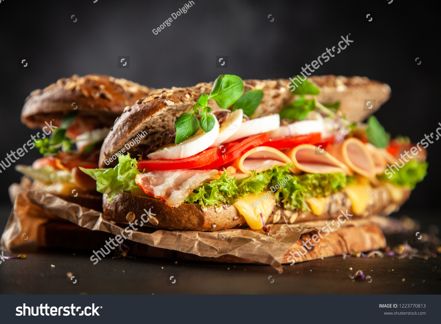 Two classic BLT sandwiches on whole-grain rolls with bacon, lettuce, tomato, and herbs