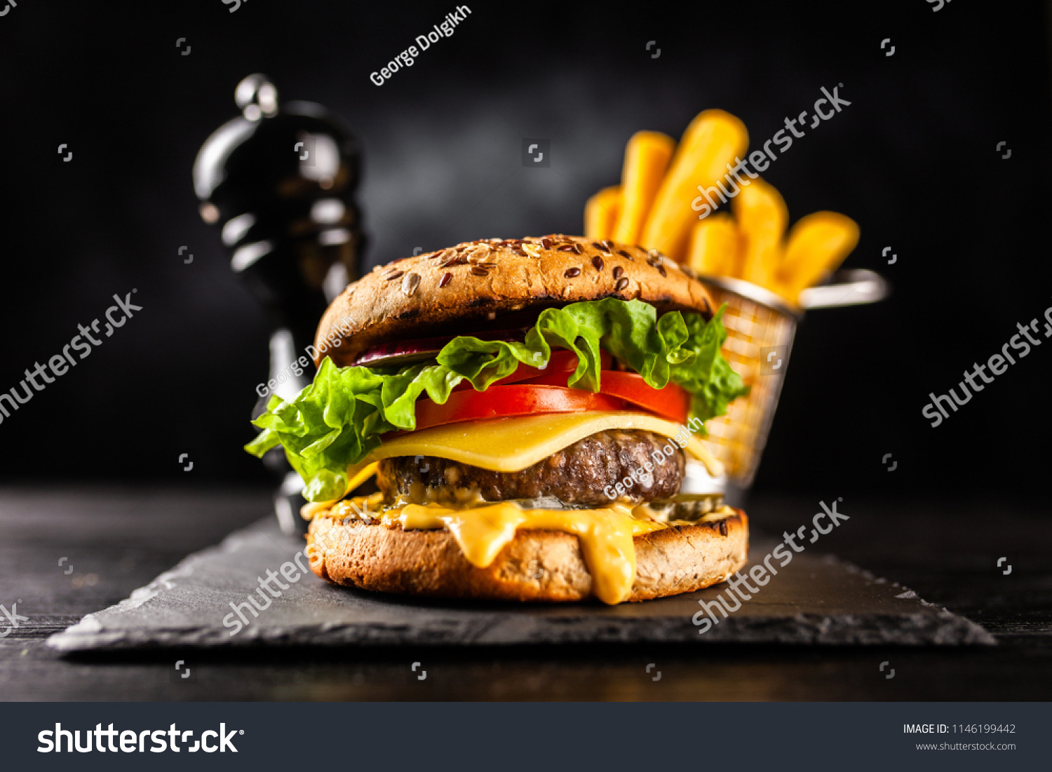 Cheeseburger with lettuce and tomato beside a basket of french fries on a dark background